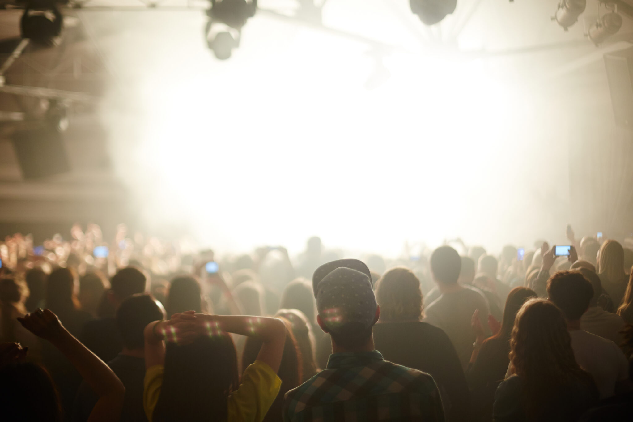 Rear view image of large crowd in front stage in bright light, watching music performance and dancing, focus on young couple in foreground